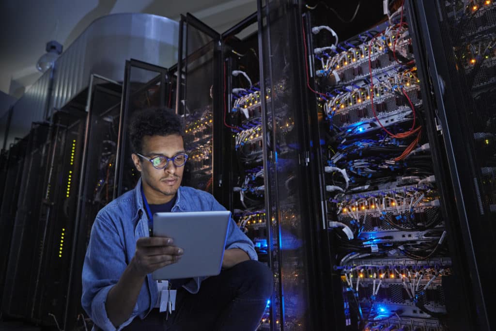 Focused male IT technician using digital tablet in dark server room